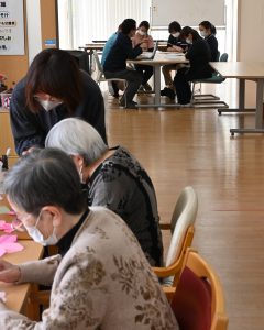 折り紙をしている小規模多機能ホームせとうちの郷のご利用者様と、奥の部屋でミーティングをしている職員。